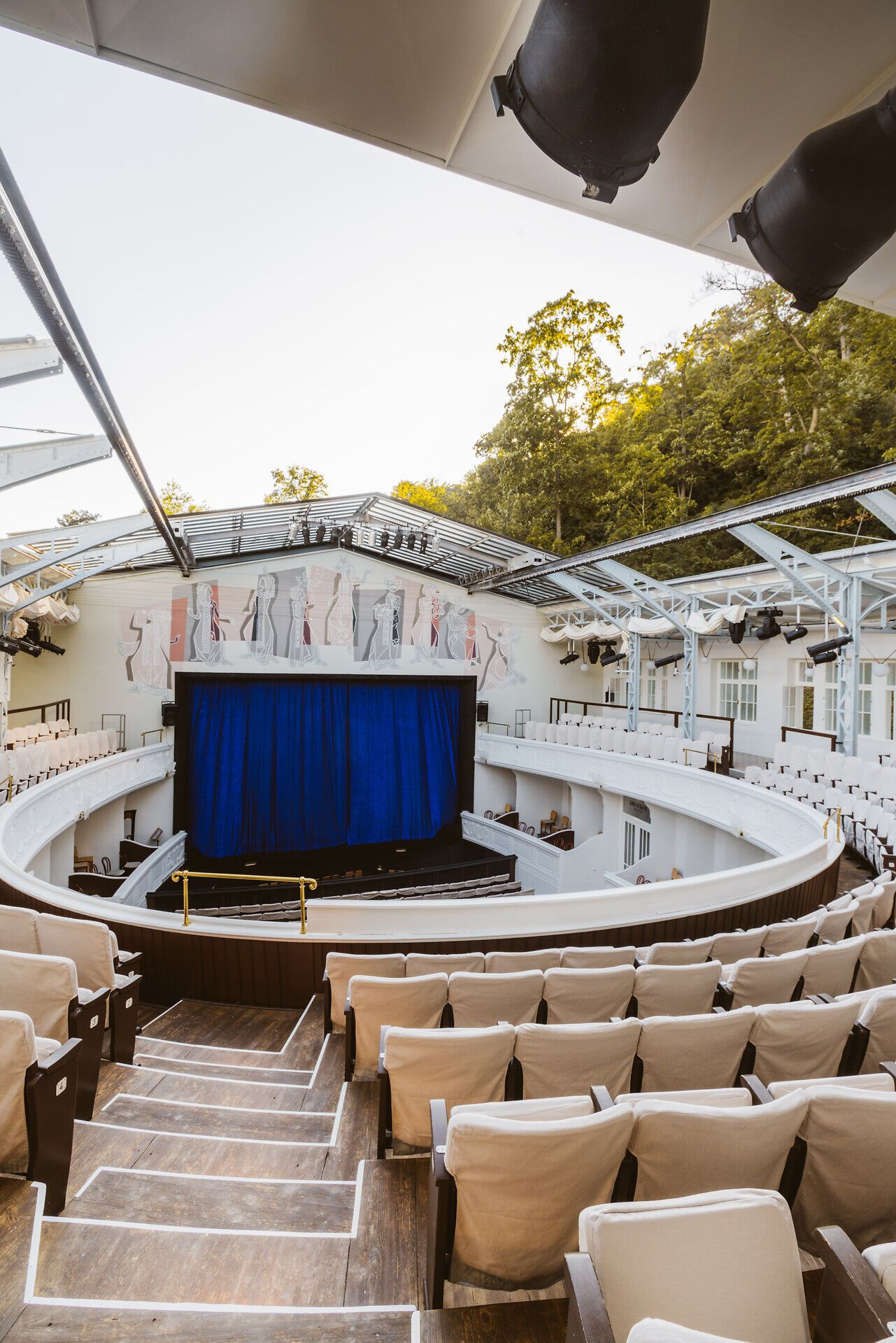 Inmitten der malerischen Kulisse des Wienerwaldes entfaltet sich ein Ort voller kultureller Höhepunkte. Die elegante Theaterbühne mit ihrem tiefblauen Vorhang lädt dazu ein, in die Welt der darstellenden Kunst einzutauchen und unvergessliche Momente zu erleben. Die gemütlichen Sitzplätze versprechen eine intime Atmosphäre, die das Festival zu einem besonderen Erlebnis macht.