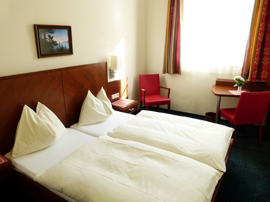 Ein Hotelzimmer mit zwei Einzelbetten, roten Stühlen und einem kleinen Tisch am Fenster.