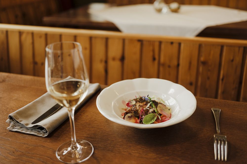 Ein Glas Weißwein neben einem Teller mit einem dekorativen Gericht auf einem Holztisch.