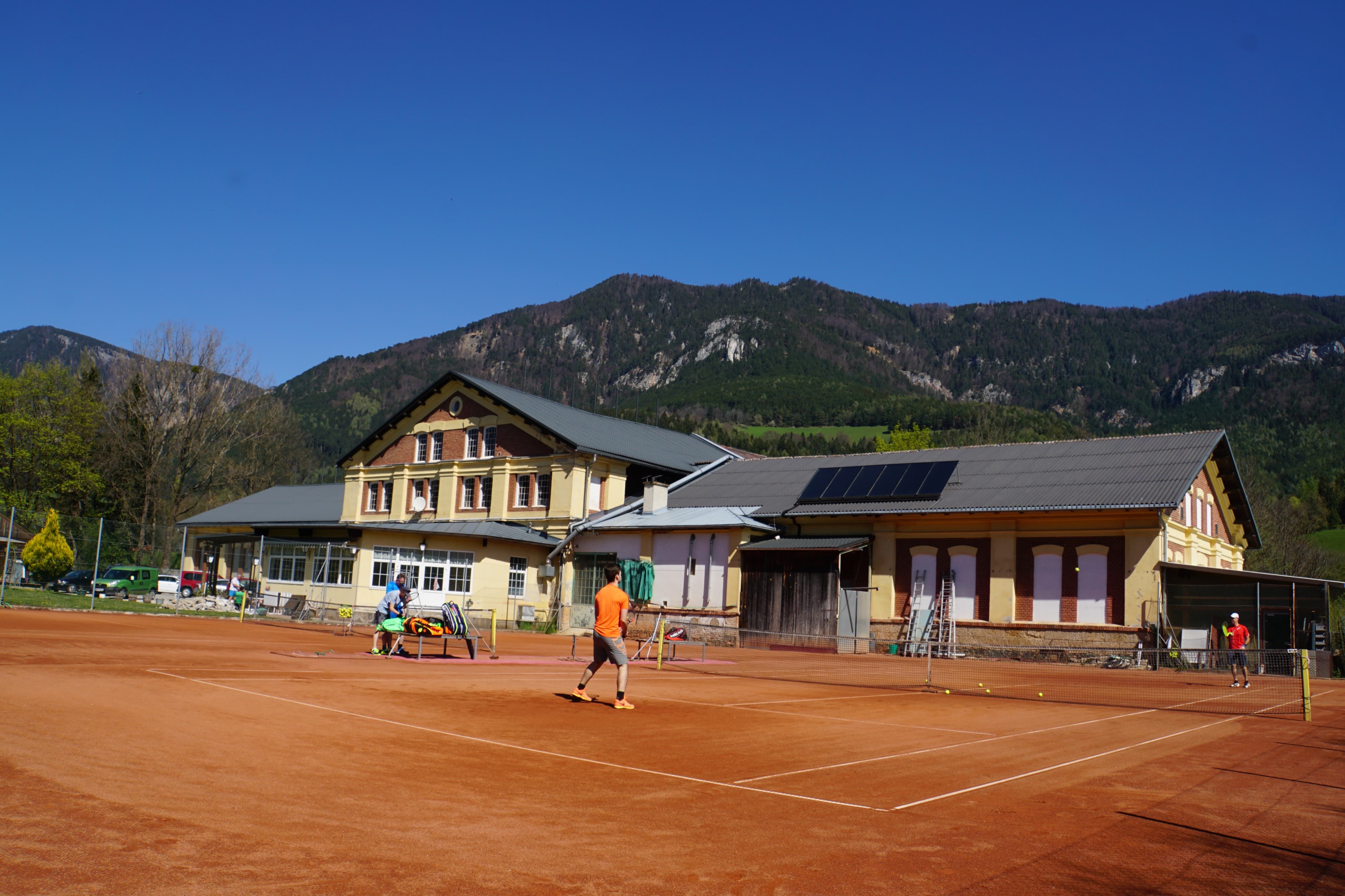 Tennisplatz vor einem Gebäude mit Bergen im Hintergrund.