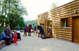 Menschen vor einem modernen Holzgeb&auml;ude in einer Waldumgebung.