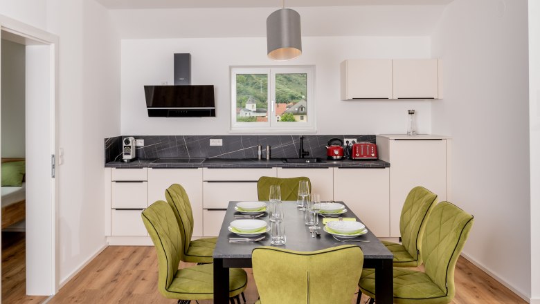 Moderne K&uuml;che mit Esstisch und gr&uuml;nen St&uuml;hlen, Fenster mit Blick auf H&uuml;gel.