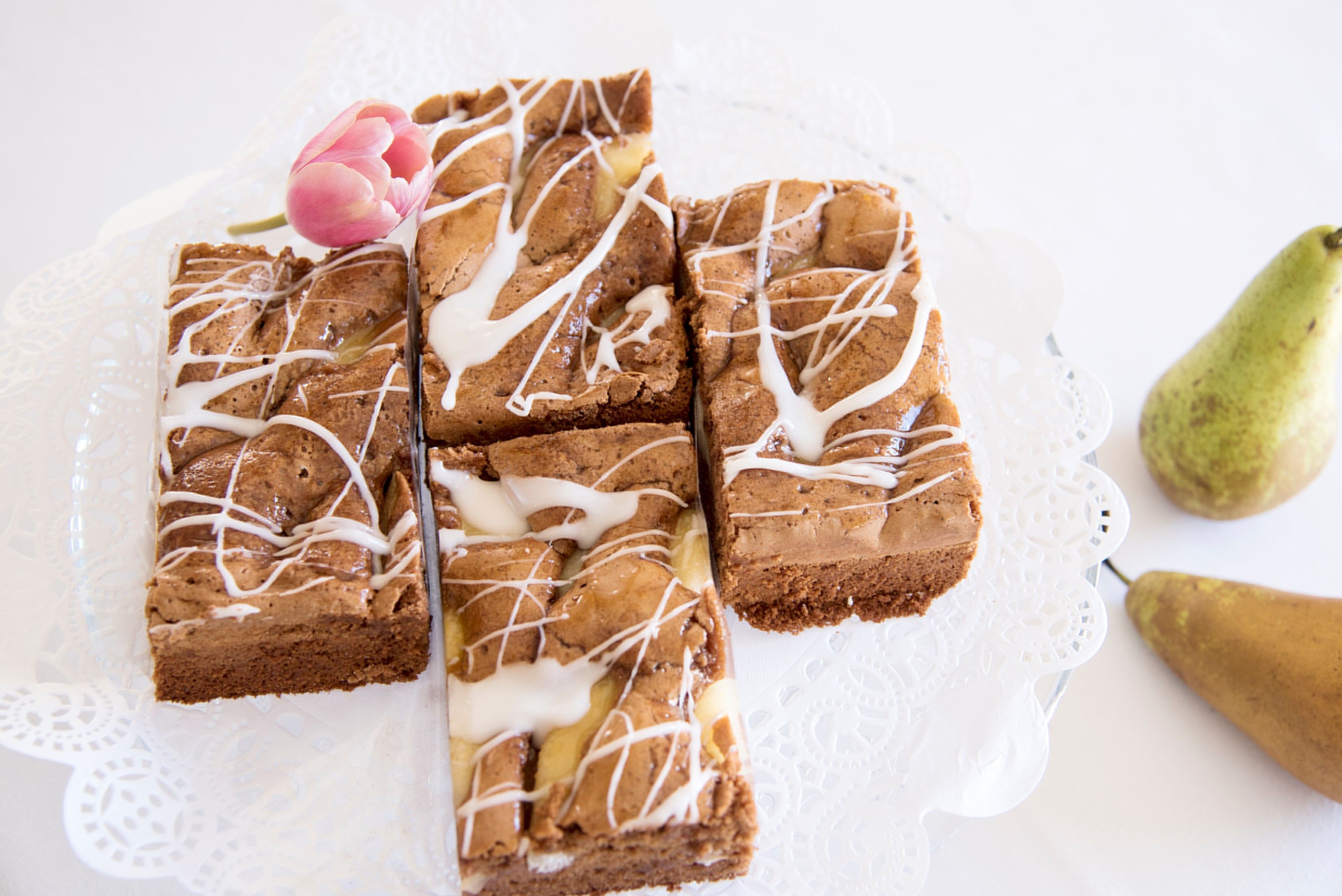 Hausgemachte Mehlspeise mit Zuckerguss und Tulpe als Dekoration, daneben Birnen.