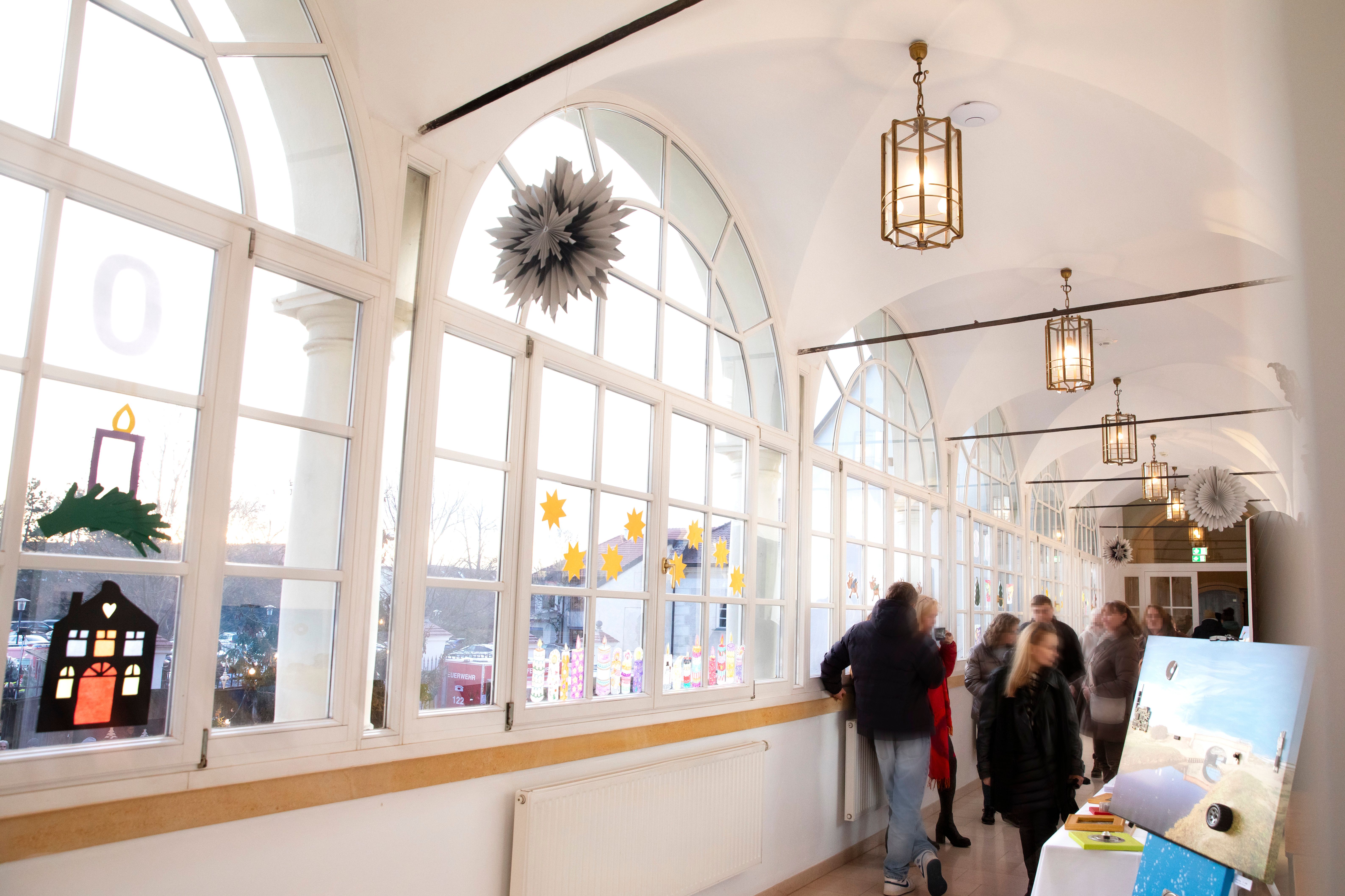 Ein heller Korridor im Schloss mit großen Fenstern und einem Stand am Christkindlmarkt mit Kunst.