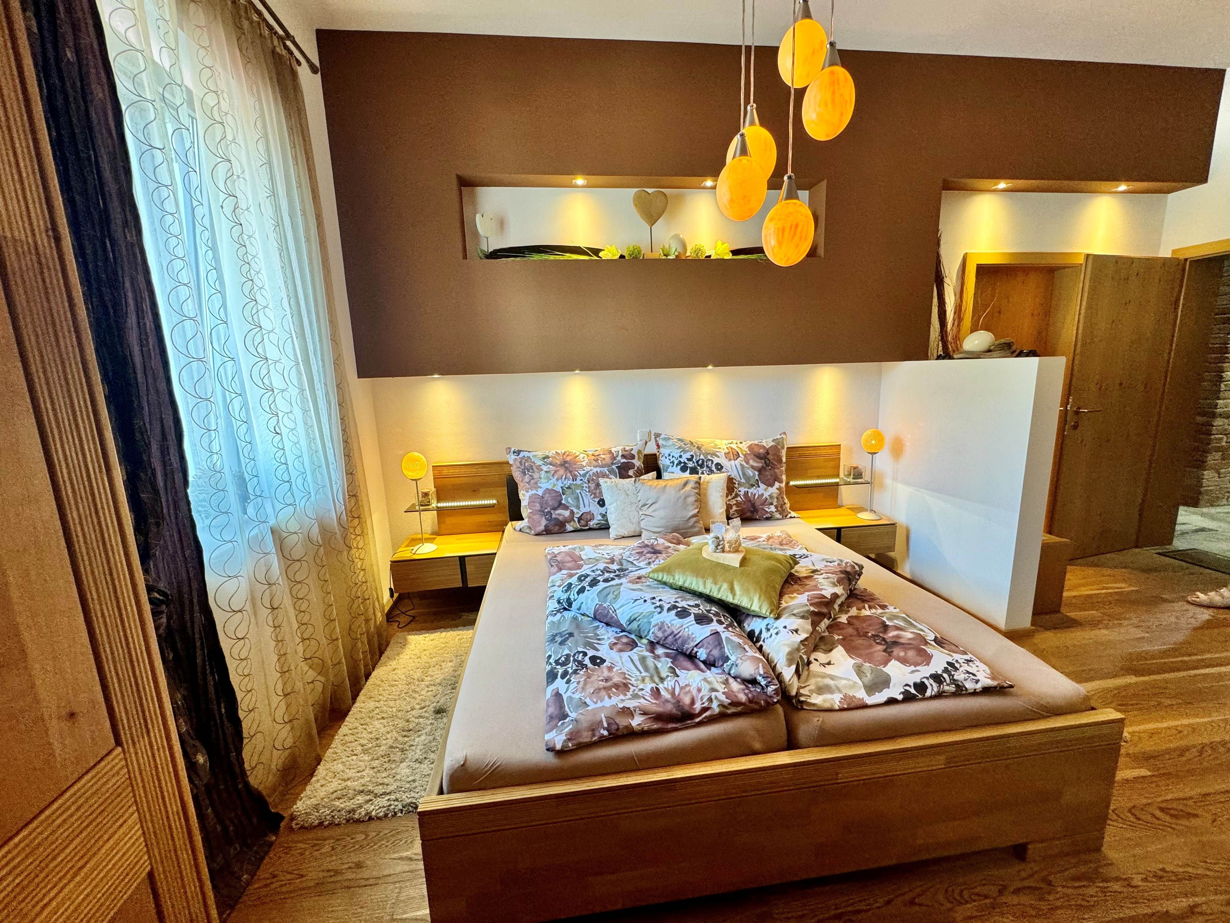 Gemütliches Schlafzimmer mit Doppelbett, dekorativen Kissen und warmem Licht, das durch die Straußeneierlampen den Raum erfüllt.