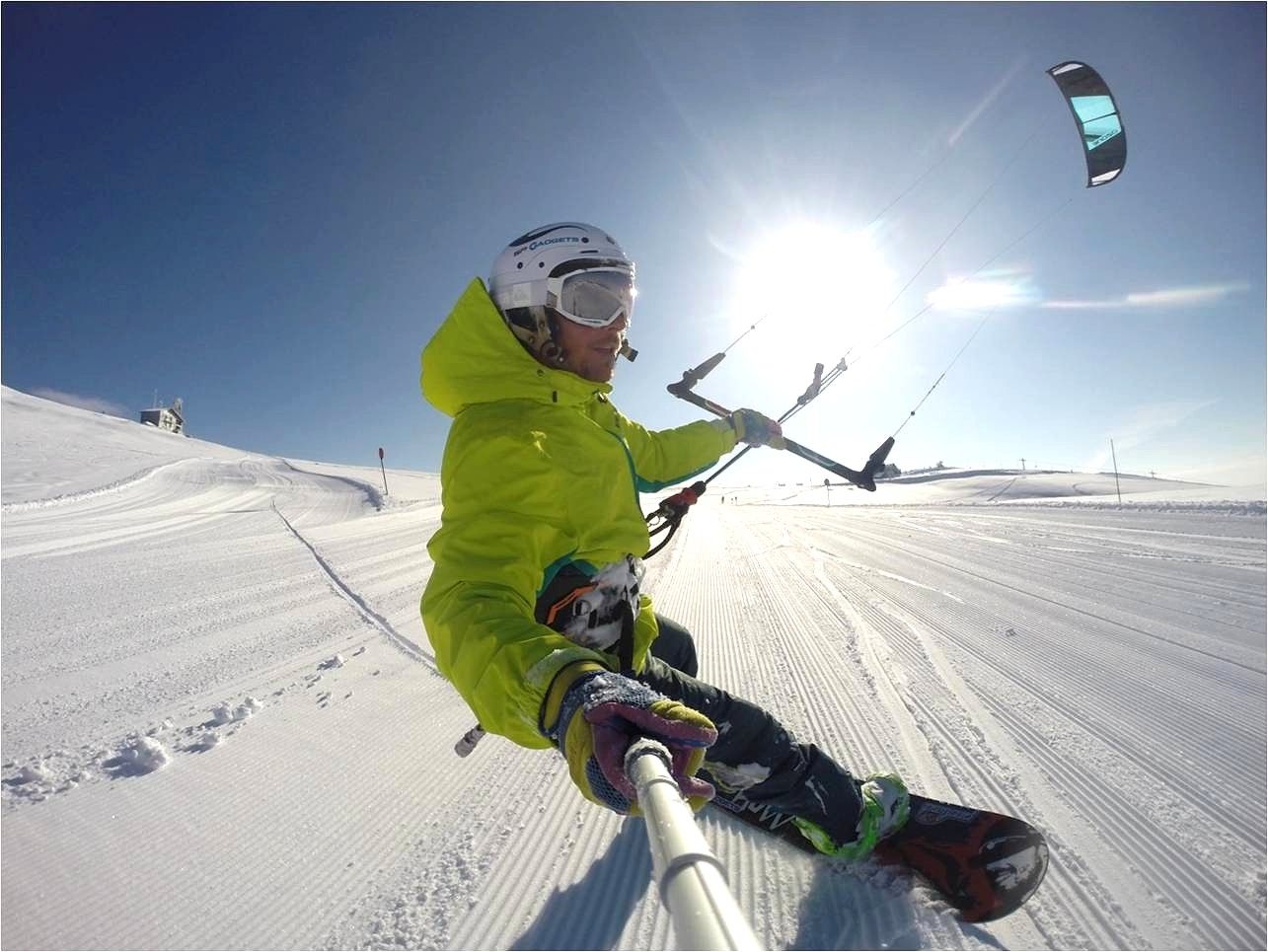 Person beim Snowkiten auf einer verschneiten Piste mit blauem Himmel und Sonnenschein.