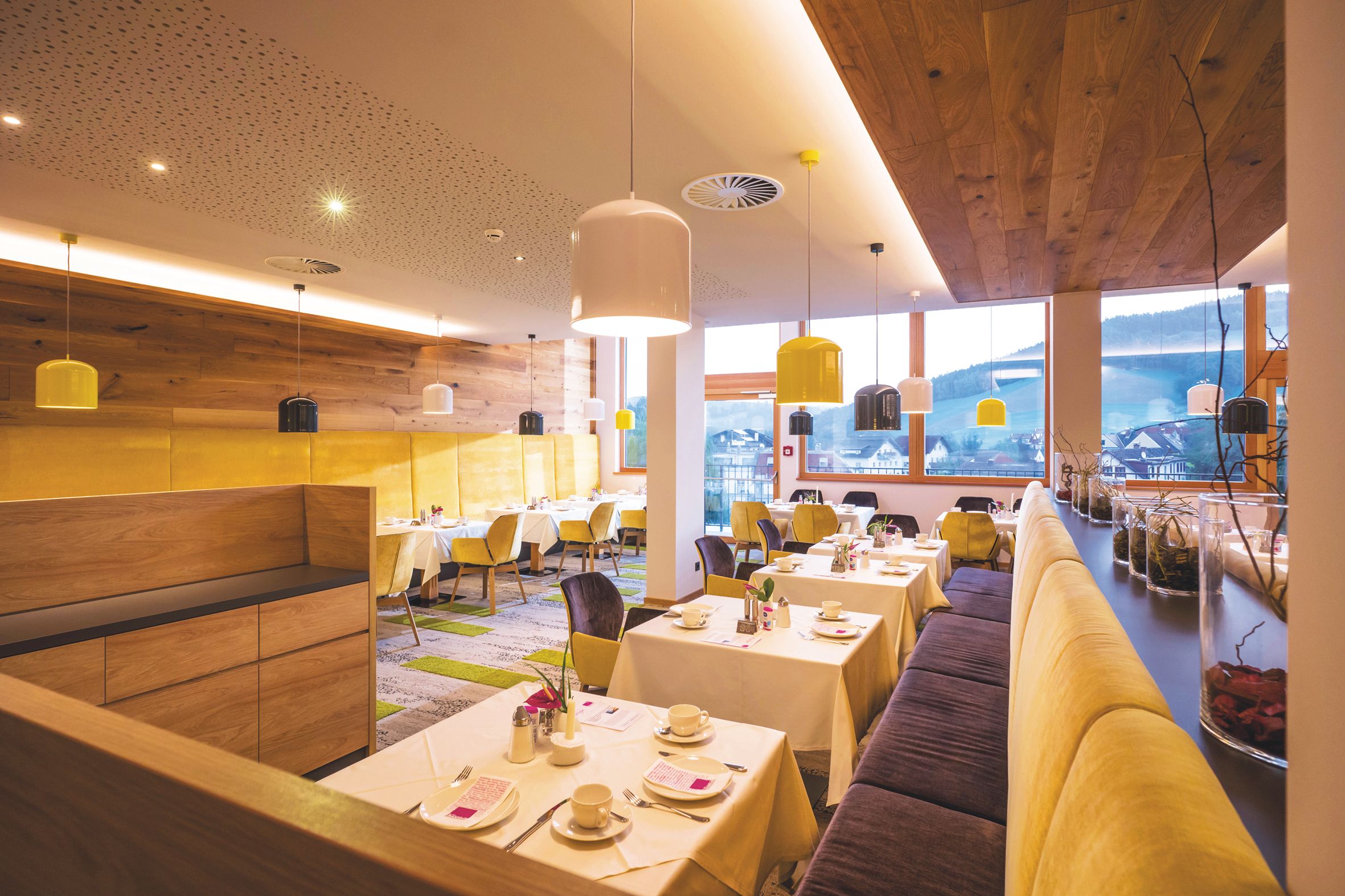 Modernes Restaurant mit Holzwänden, gelben Stühlen und bunten Lampen.