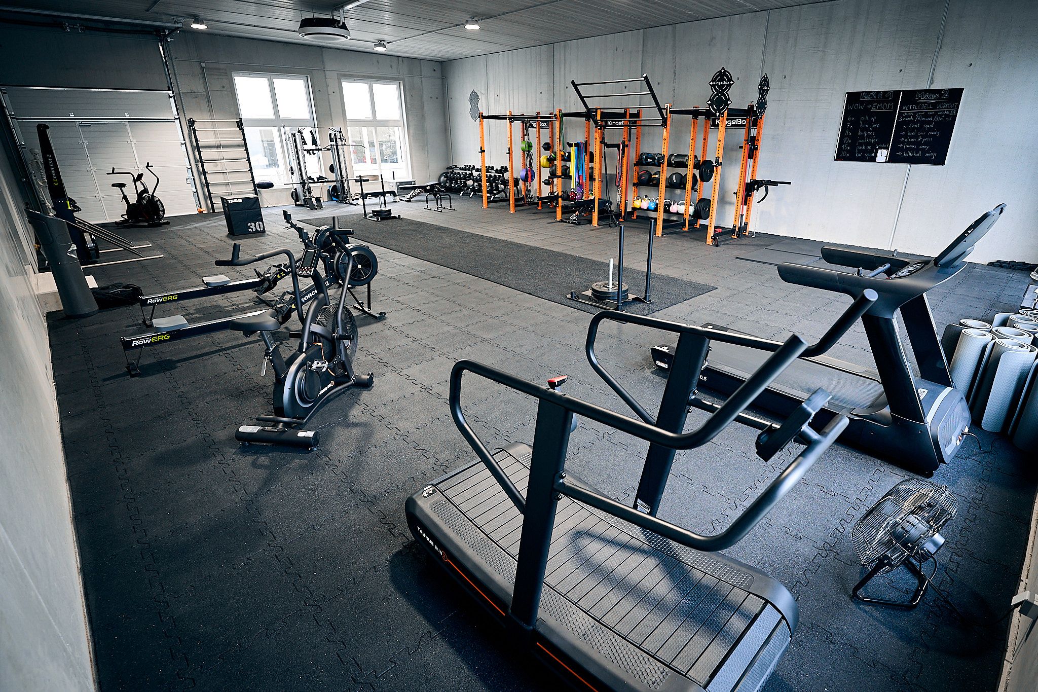 Innenansicht eines Fitnessstudios mit verschiedenen Trainingsgeräten wie Laufbänder, Fahrräder und Hanteln.
