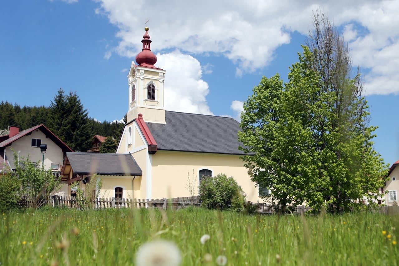 Kirche in Mitterbach mit rotem Turm und grünem Baum im Vordergrund.