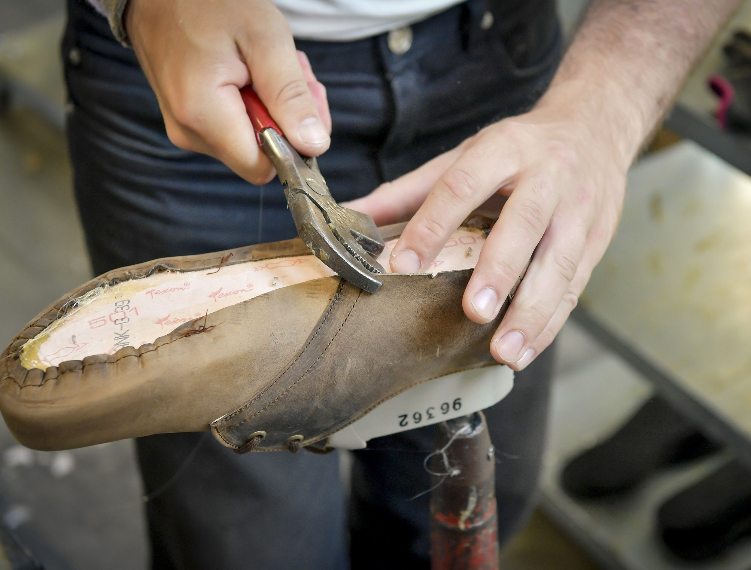 Person bearbeitet Schuh mit Zange auf einem Leisten.
