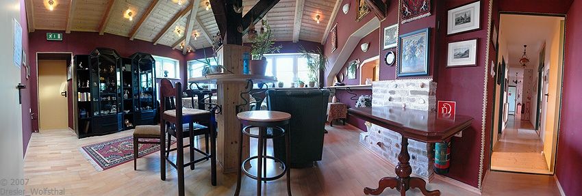 Gemütlicher Clubraum mit Holzmöbeln, Teppich und Bildern an den Wänden.