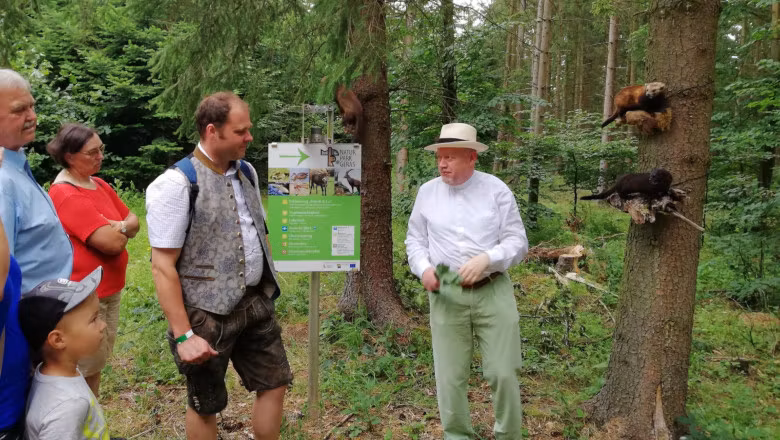 Gruppe von Menschen im Wald, die einem Mann zuhören, der vor einem Schild im Naturpark Geras steht.