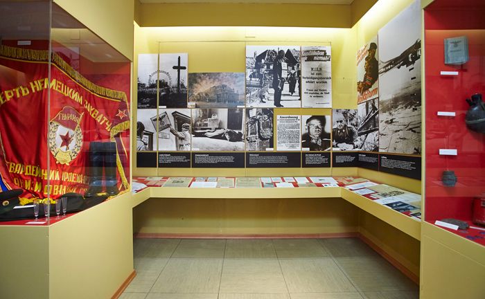 Ausstellungsraum mit historischen Fotos, Dokumenten und einer roten Fahne.