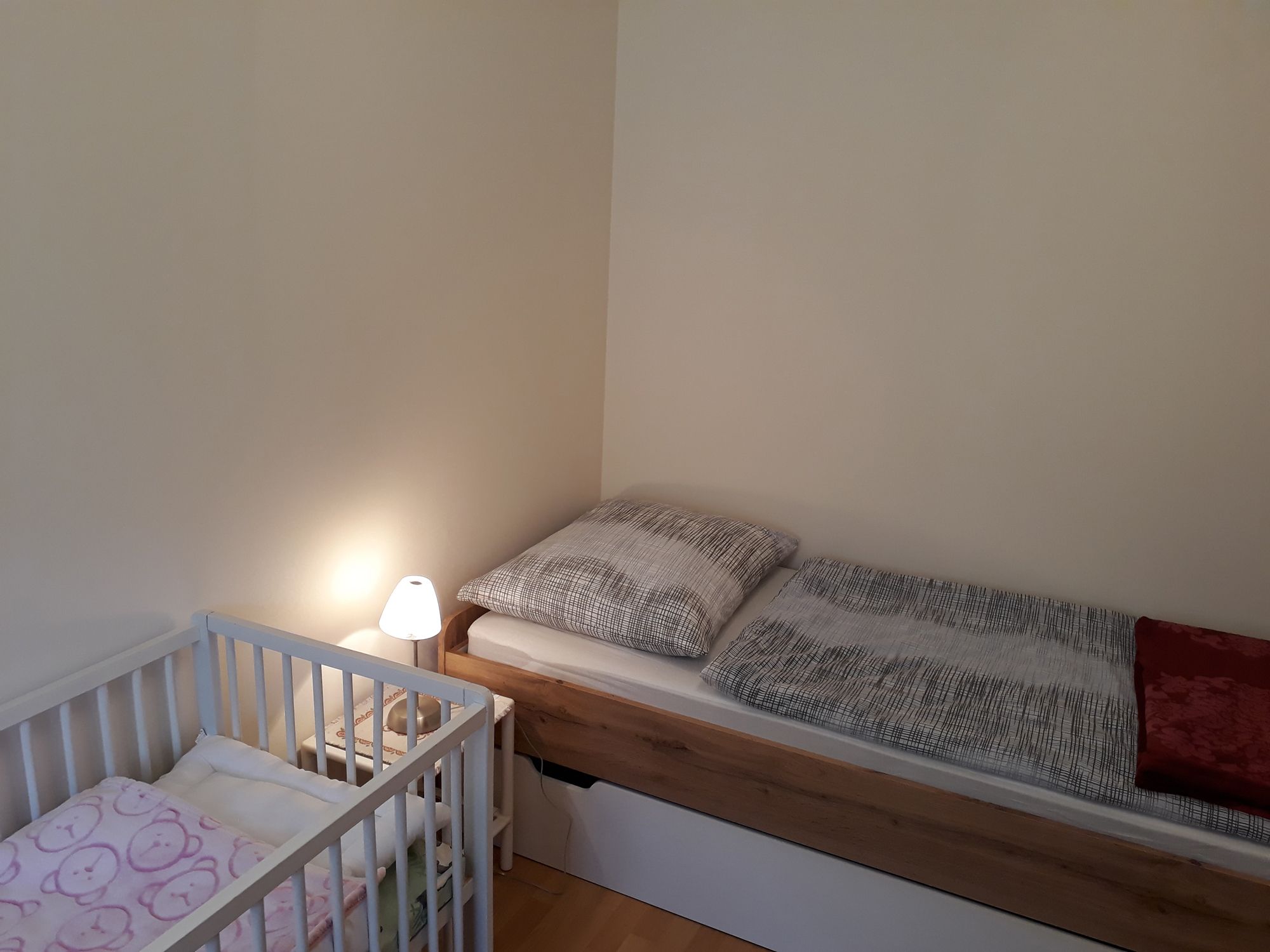 Einzelzimmer mit Einzelbett, Kinderbett und Nachttischlampe.