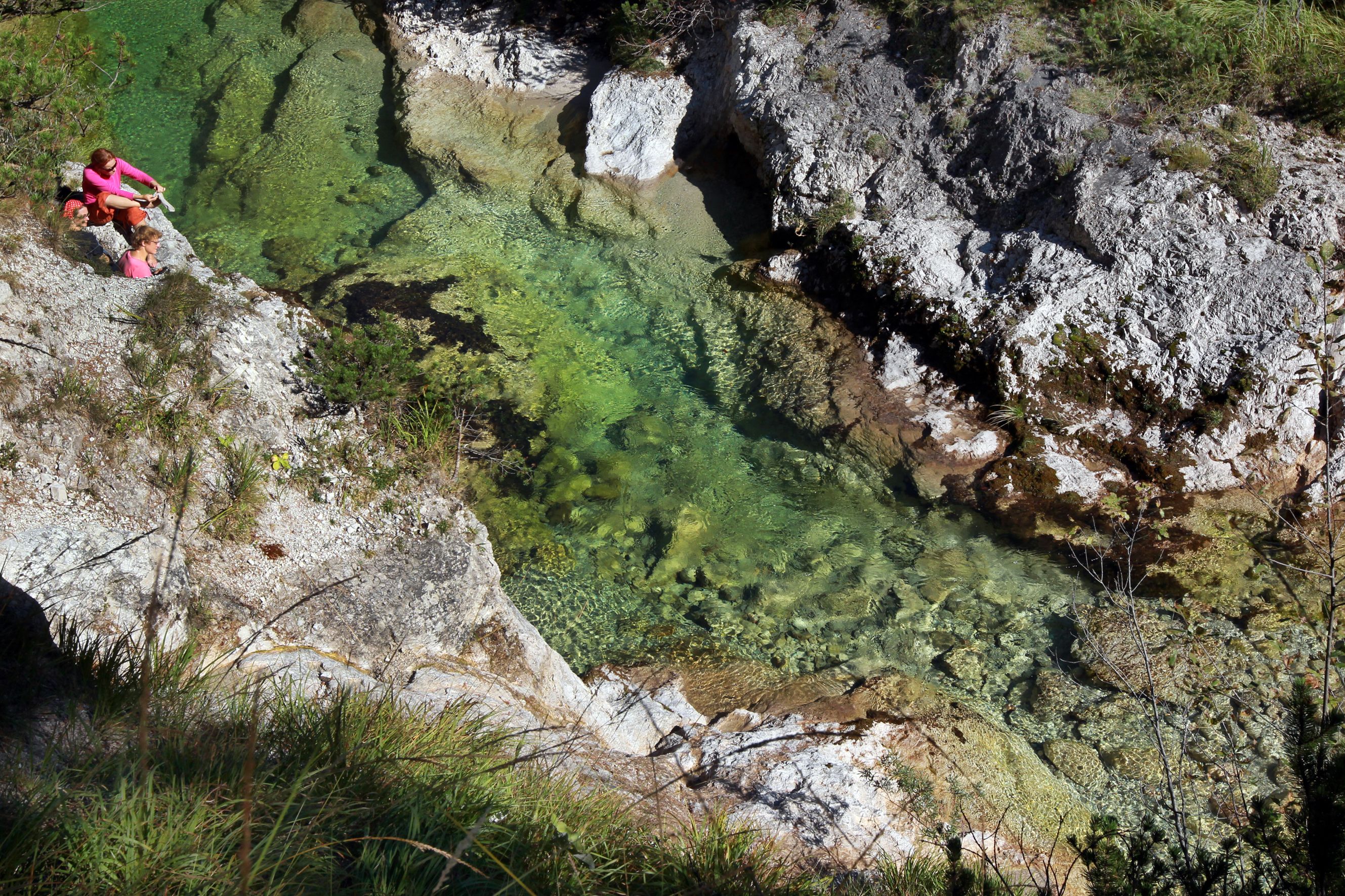 Zwei Personen sitzen auf einem Felsen neben einem klaren, grünen Fluss in einer Schlucht.