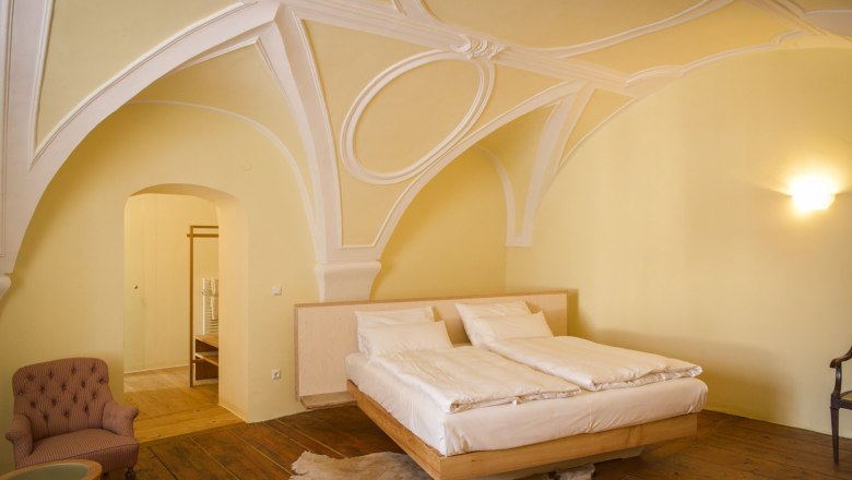 Gut Oberstockstall, © Robert Herbst Ein elegantes Schlafzimmer mit gewölbter Decke, einem Doppelbett, einem Sessel und Holzboden.