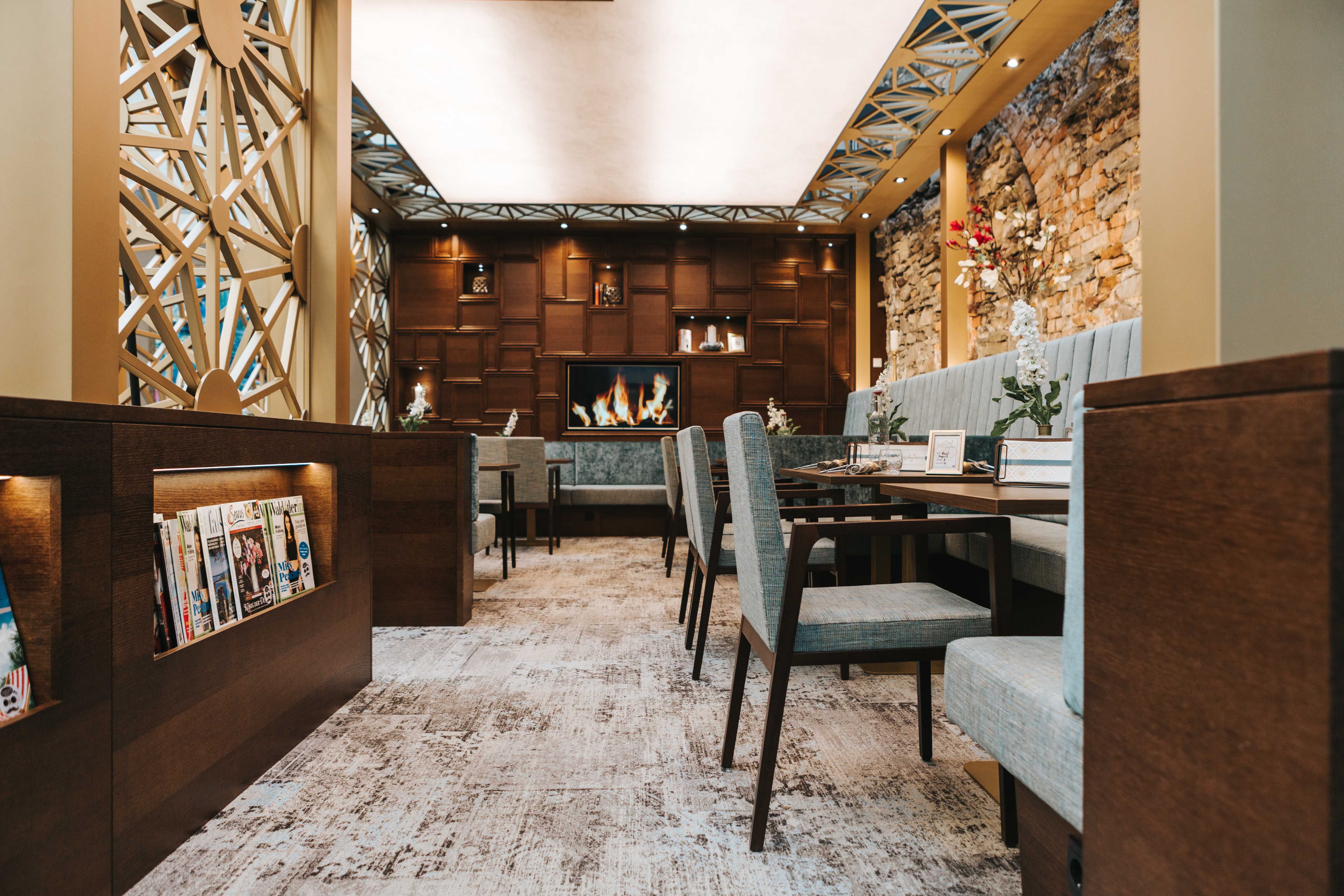 Innenansicht eines stilvollen Cafés mit gemütlichen Sitzgelegenheiten, Kamin und Zeitschriftenregal.