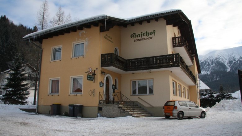 Ein gelbes Geb&auml;ude mit der Aufschrift 'Gasthof Sonnenhof' im Schnee, umgeben von Bergen.