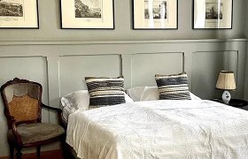 Schlafzimmer mit Doppelbett, antikem Stuhl und gerahmten Bildern an der Wand.