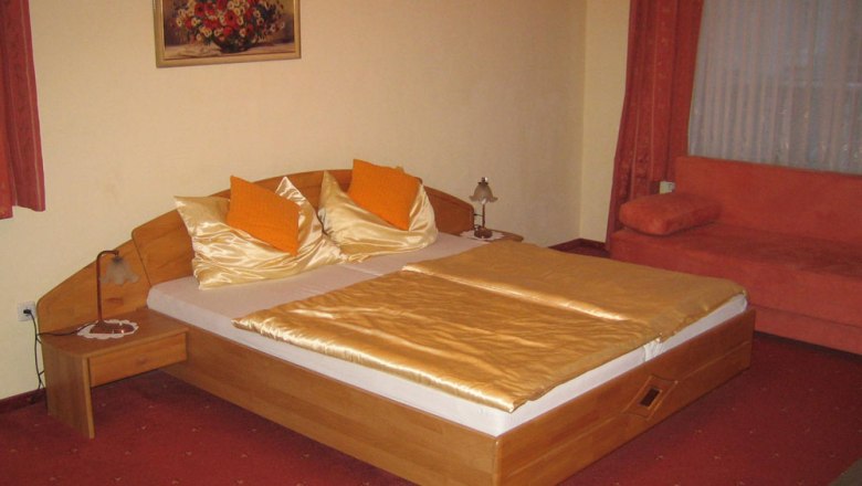 Gemütliches Hotelzimmer mit Doppelbett, orangen Kissen und Deckenleuchten.