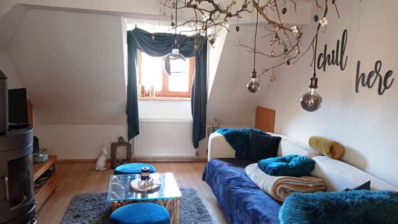 Gem&uuml;tliches Wohnzimmer mit Sofa, blauem Teppich, Dekozweigen und Schriftzug 'chill here'.