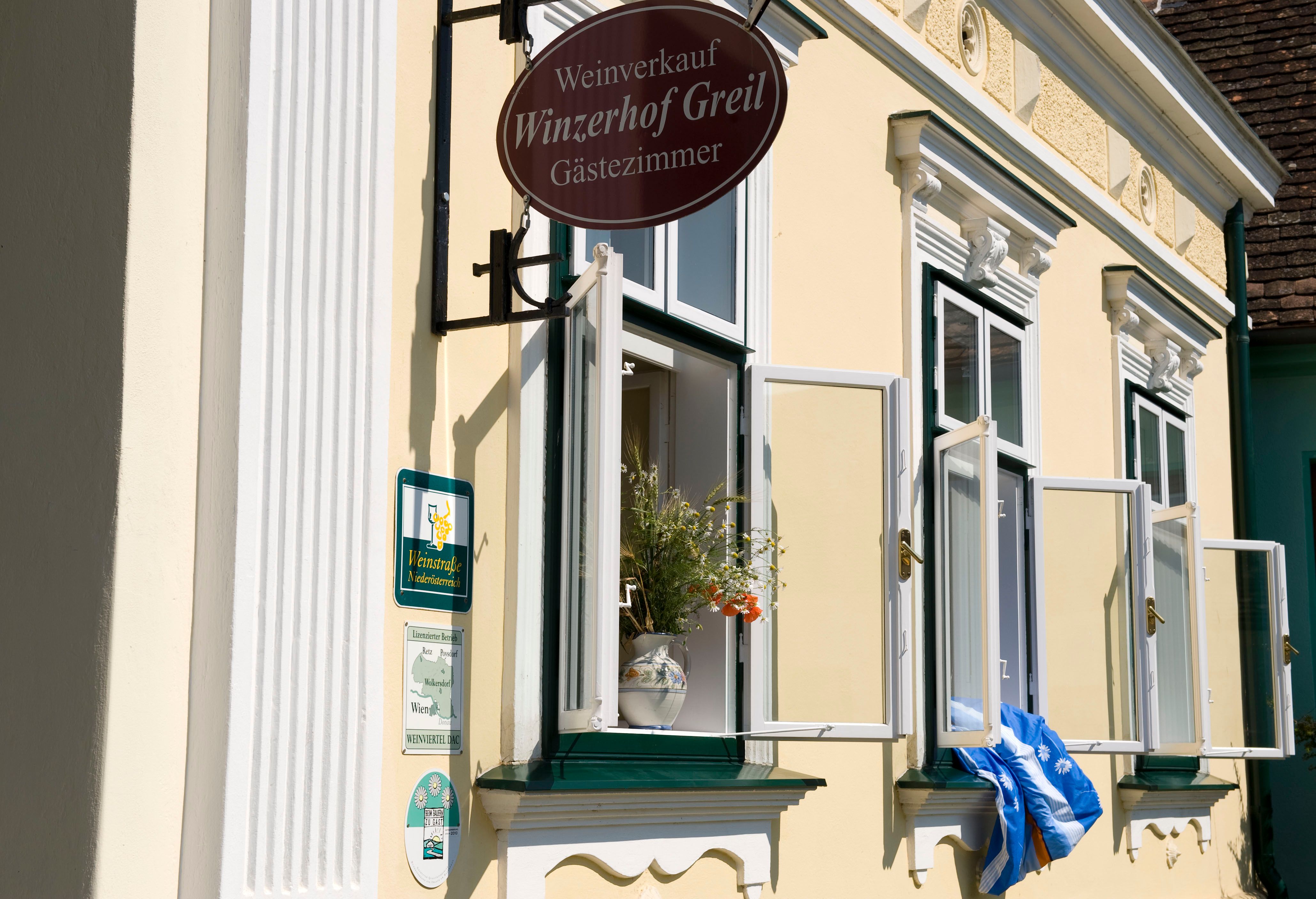 Fassade eines gelben Gebäudes mit geöffneten Fenstern und einem Schild 'Winzerhof Greil'.
