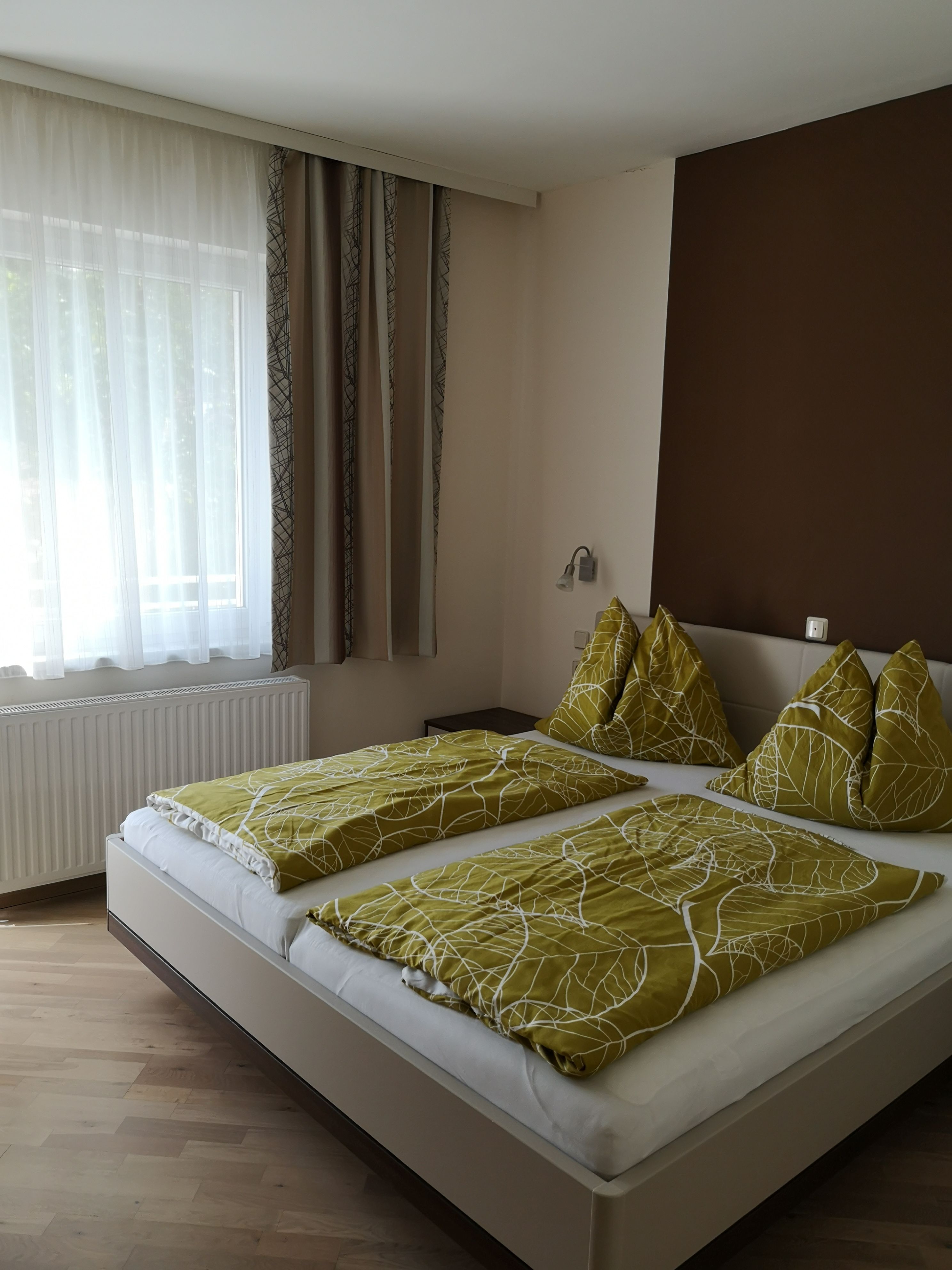 Ein Doppelzimmer mit einem Bett, grüner Bettwäsche und einem Fenster mit Vorhängen.