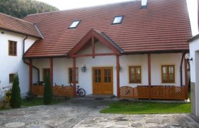 Ein traditionelles Gebäude mit rotem Ziegeldach und Holzelementen, umgeben von einem gepflasterten Hof.