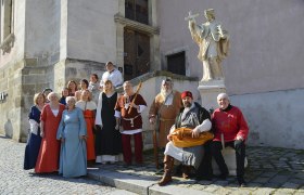 Gruppe von Menschen in mittelalterlicher Kleidung vor einer Statue in einer Altstadt.