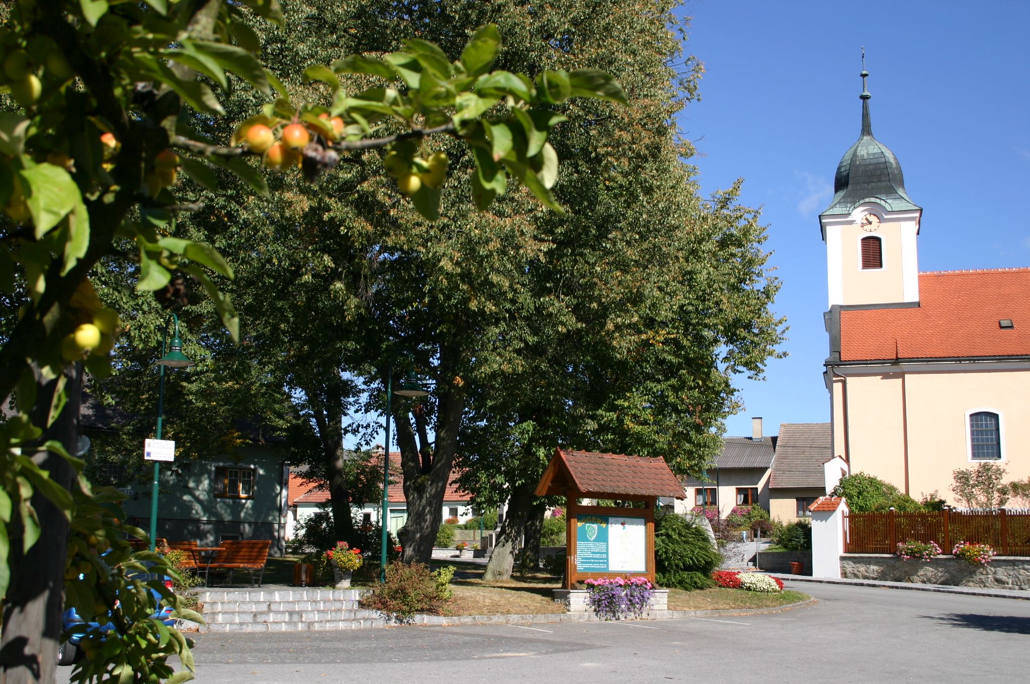 Dorfplatz mit Kirche, Bäumen und Infotafel in Eggern.