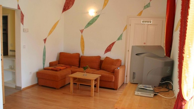 Wohnzimmer mit oranger Couch, Holztisch, Fernseher und bunter Wanddekoration.