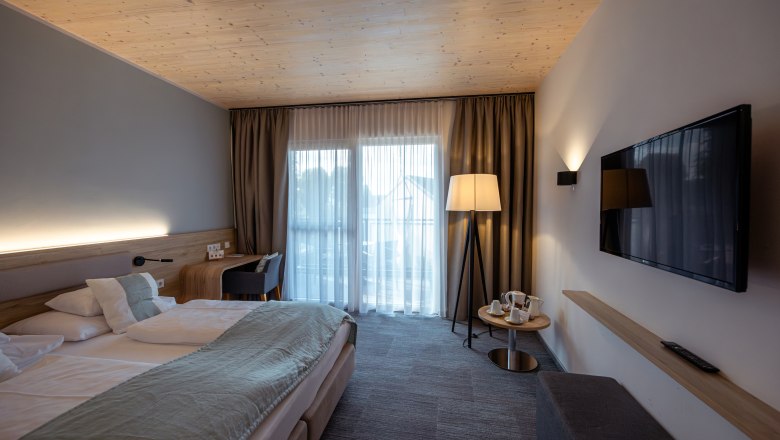 Modernes Hotelzimmer mit Doppelbett, Fernseher, Stehlampe und Balkon.