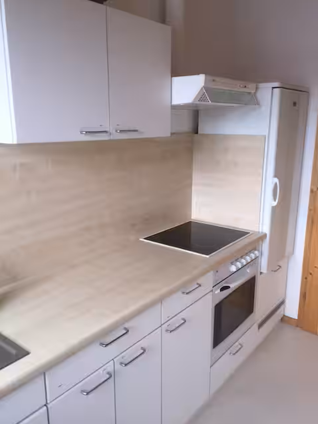 Helle Küche mit großem Kühlschrank, Backofen, Spüle und Ceranfeld.