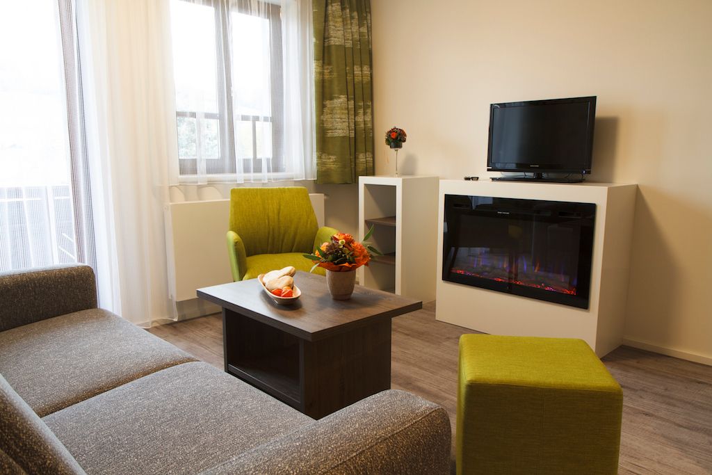 Moderner Wohnbereich mit Sofa, grünem Sessel, Couchtisch, Kamin und Fernseher.