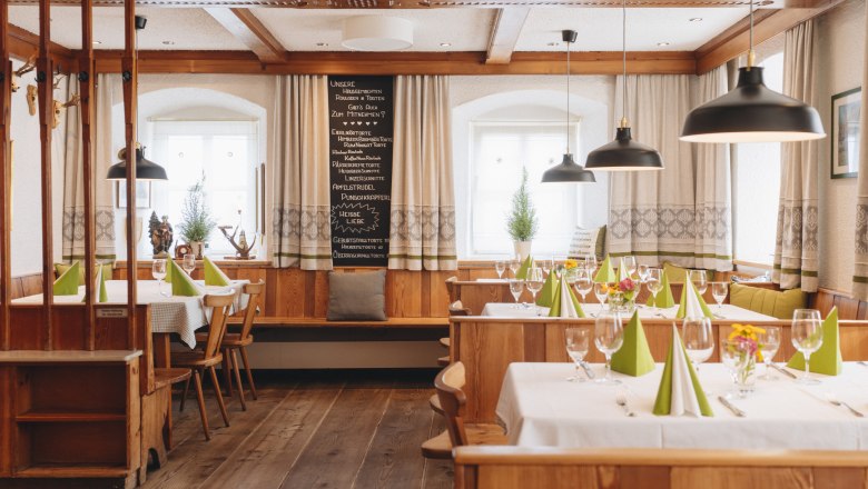 Gem&uuml;tliche, traditionelle Gaststube mit Holzm&ouml;beln, gedeckten Tischen und gr&uuml;nen Servietten.