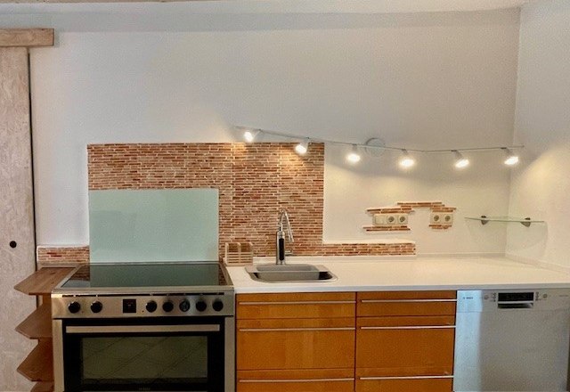 Moderne K&uuml;che mit Herd, Sp&uuml;le und Geschirrsp&uuml;ler vor einer Mosaikfliesenwand.