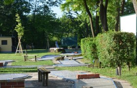 Minigolfplatz mit Bahnen und Bäumen im Hintergrund.
