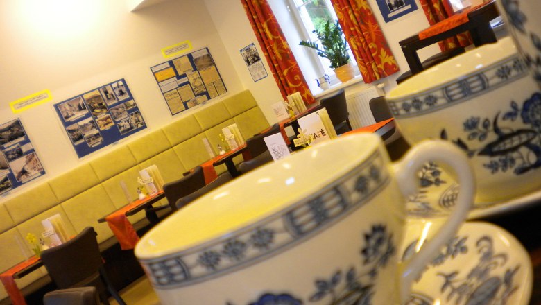 Innenansicht eines Caf&eacute;s mit Teetassen im Vordergrund und dekorierten W&auml;nden im Hintergrund.