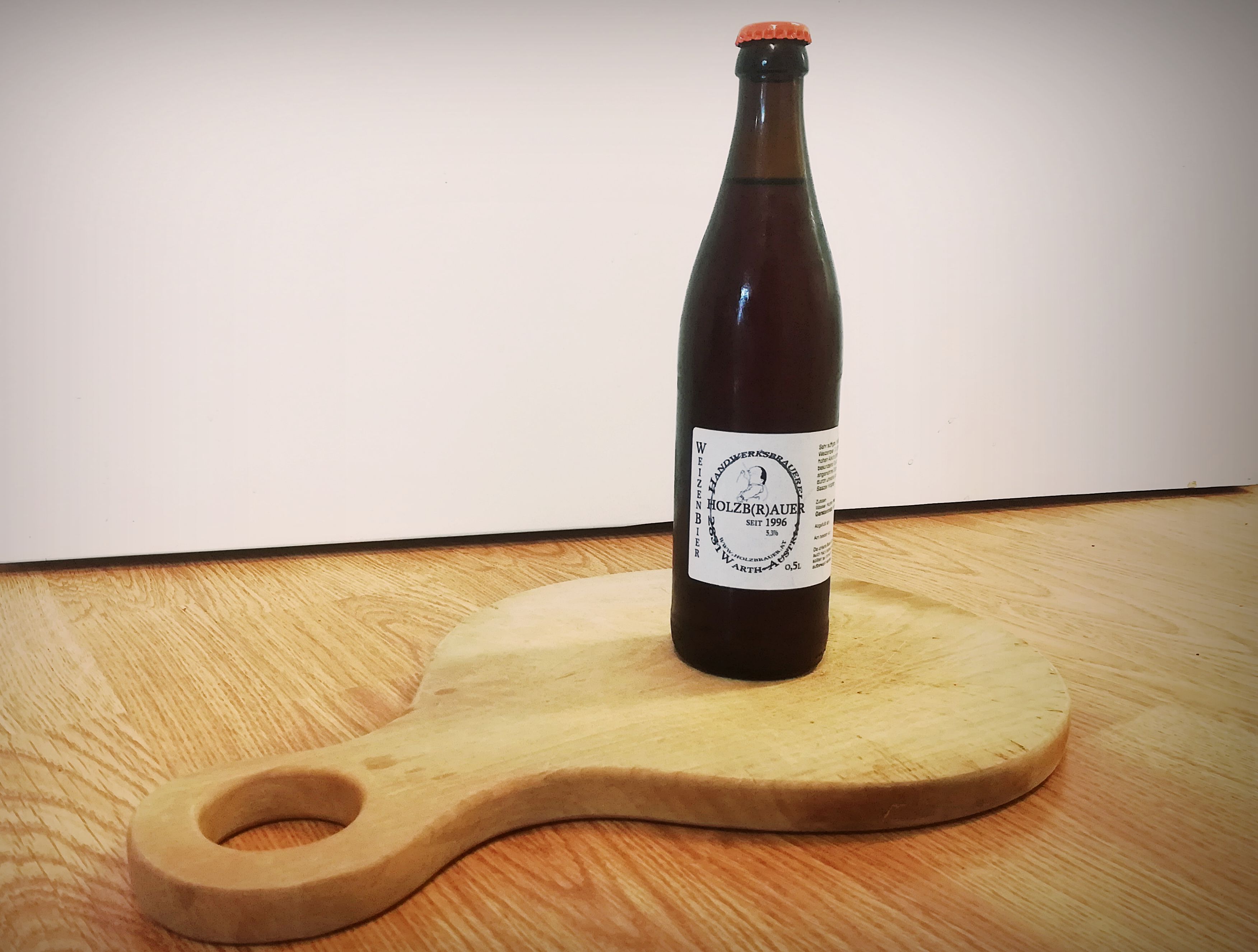 Eine Flasche Weizenbier vom Holzbräu steht auf einem runden Holzbrett mit Griff.