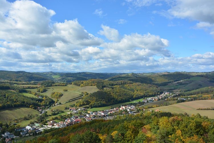 Landschaft mit Hügeln, Wäldern und einem Dorf im Herbst.