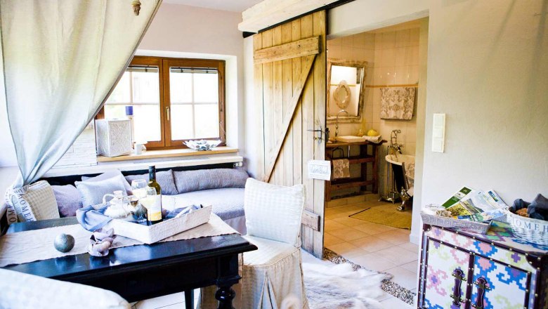 Gemütliches Wohnzimmer mit Holztür, Sofa, Tisch und dekorativen Elementen, Blick ins Badezimmer.