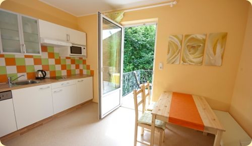 Helle Küche mit Essecke, bunter Fliesenspiegel und offener Balkontür.