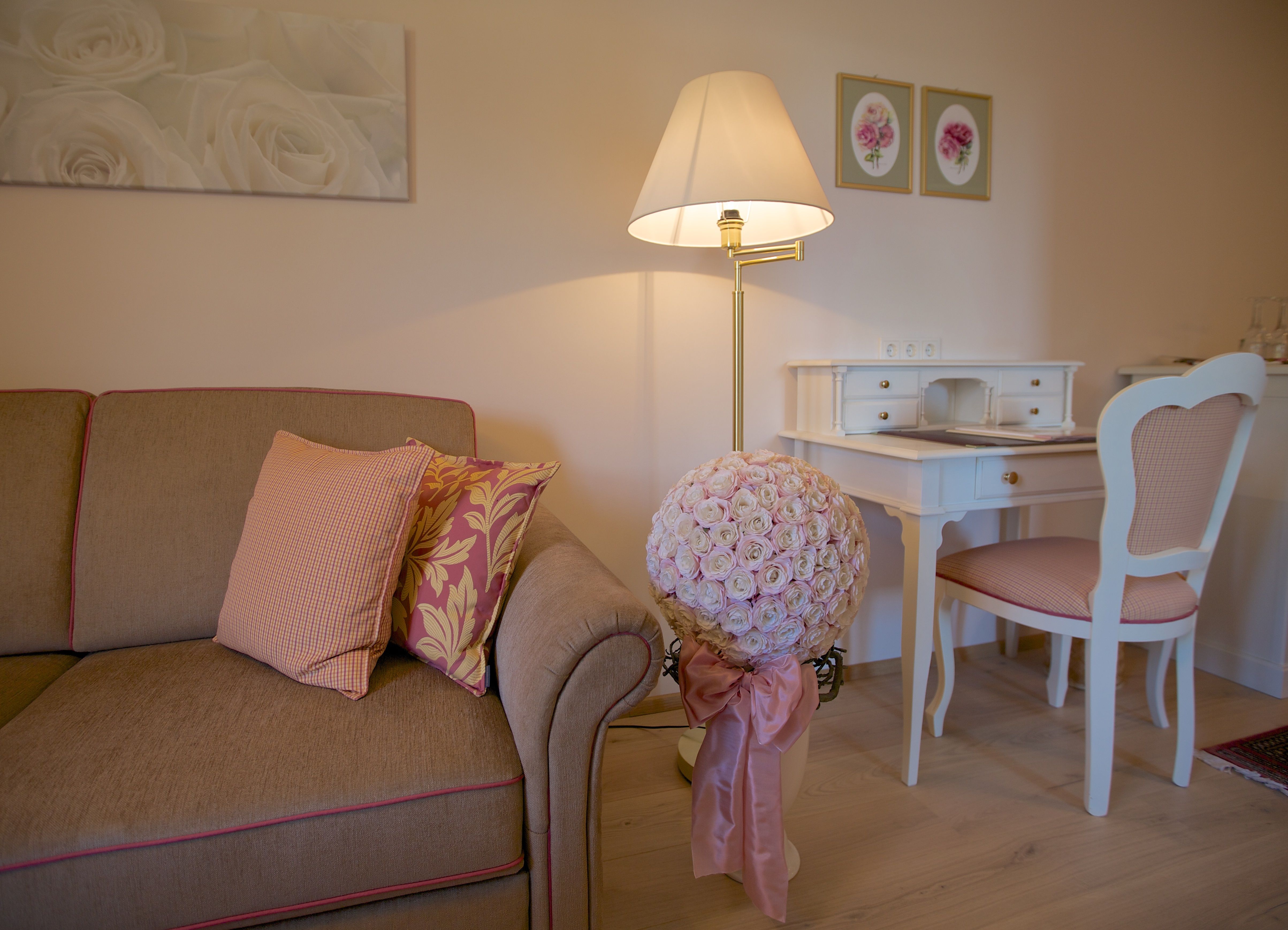 Gemütliches Wohnzimmer mit Sofa, Schreibtisch und Blumenarrangement.