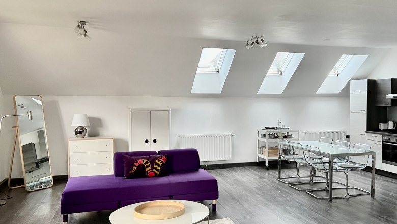 Modernes Loft mit violetten Sofas, Esstisch und Küchenzeile unter Dachfenstern.