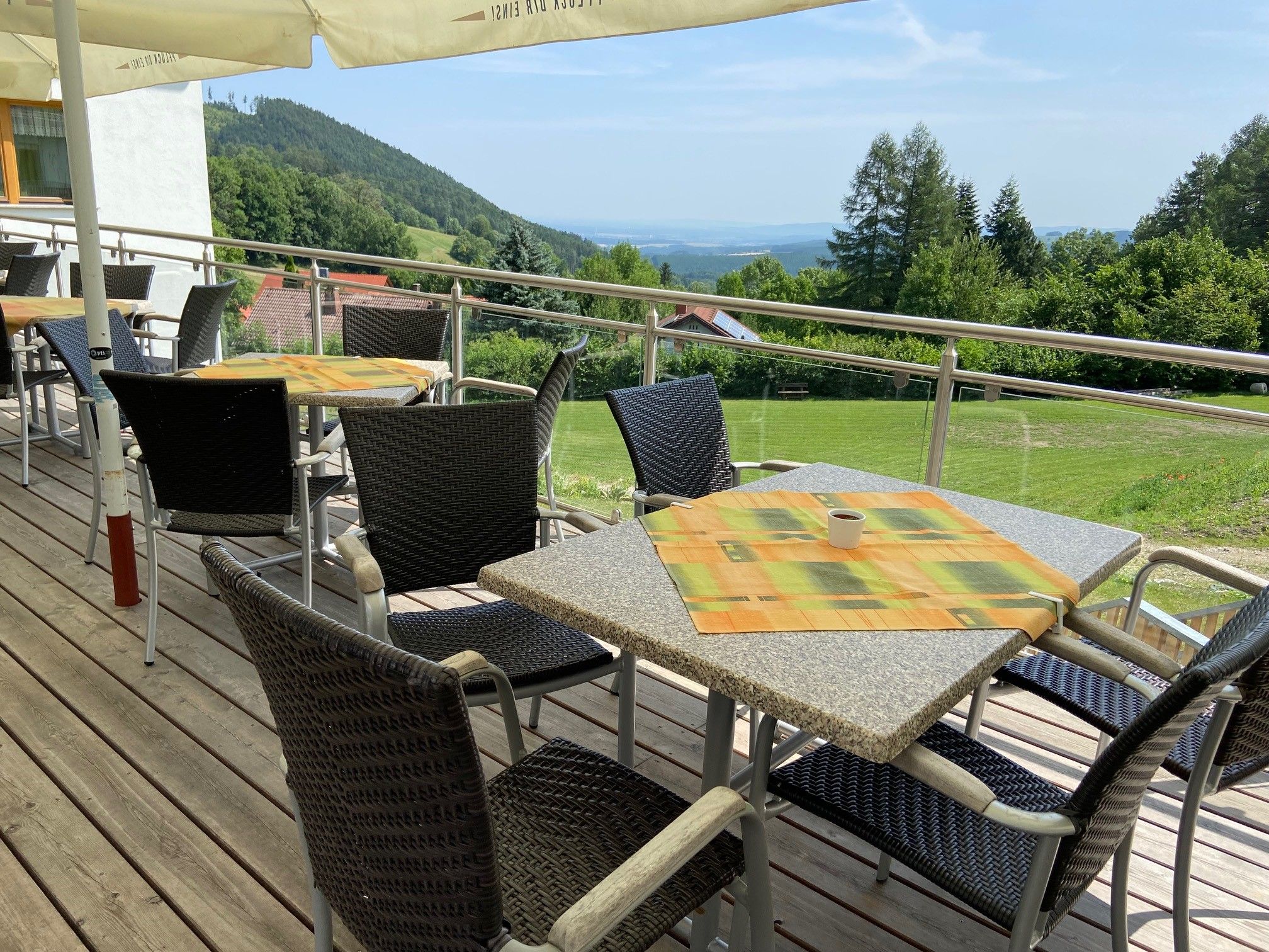 Terrasse mit Tischen und Stühlen, Blick auf grüne Hügel und Bäume im Hintergrund.