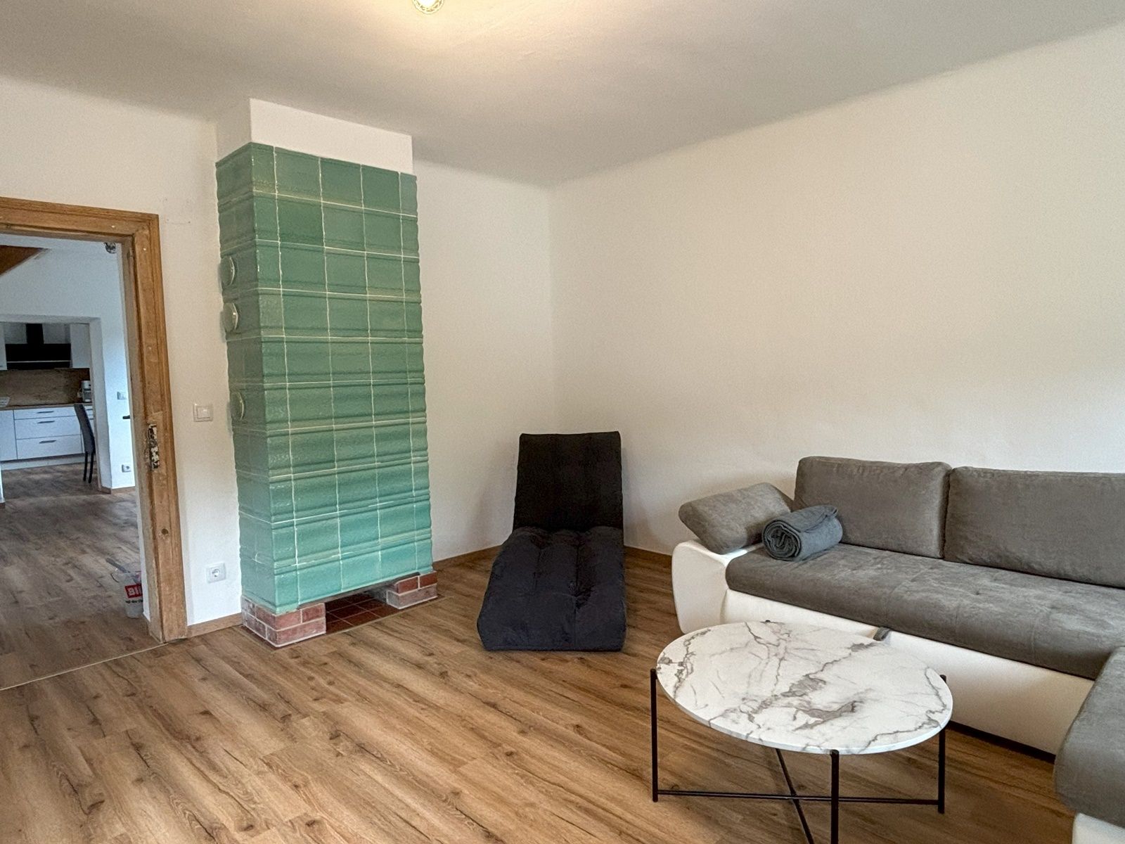 Wohnzimmer mit grauem Sofa, rundem Marmortisch und grünem Kachelofen.