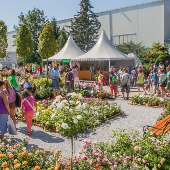 Menschen auf einer Gartenmesse mit Blumenbeeten und weißen Zelten.