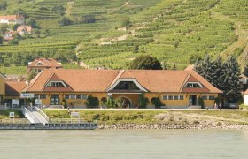 Gelbes Gebäude mit rotem Dach vor Weinbergen in Spitz an der Donau.