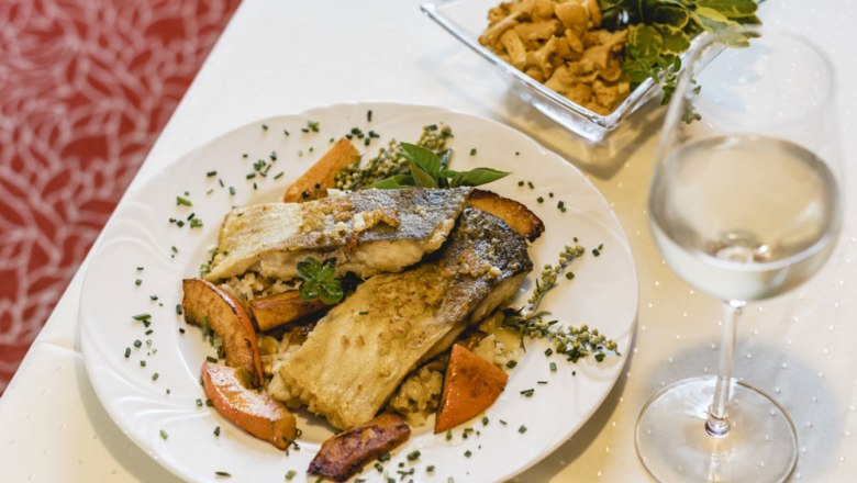 Gourmetgericht mit Fischfilet, Gemüse und Weißwein auf weißem Tisch.