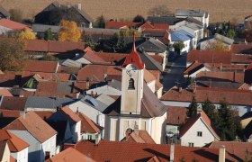 Luftaufnahme der Pfarrkirche Getzersdorf mit umliegenden H&auml;usern und Feldern im Herbst.